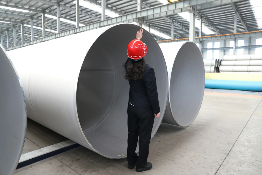 worker inspects large metal pipes in factory